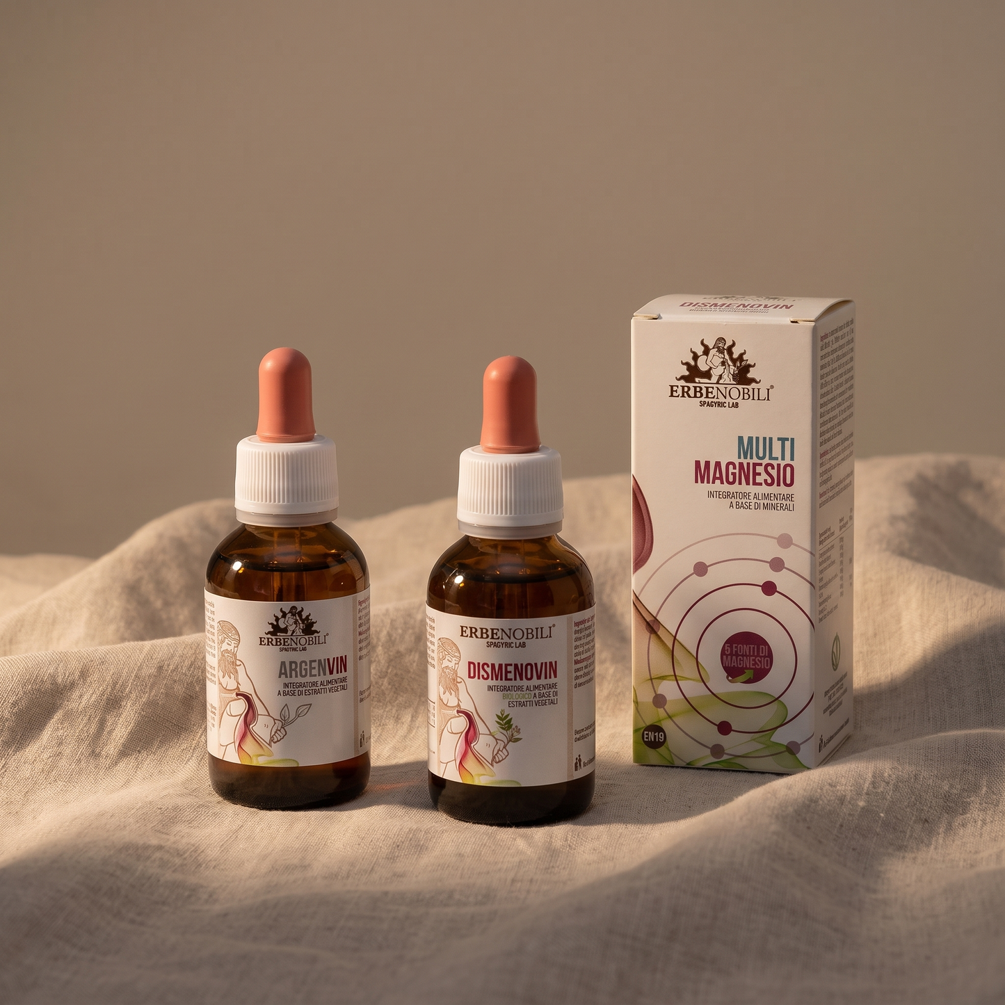 Rituale serale del Kit Dolce Ciclo: flaconi e capsule su lino chiaro in luce calda.